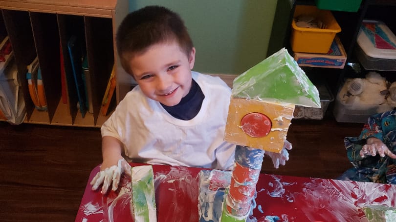 A smiling boy at In His Care proudly building a tall tower during sensory play