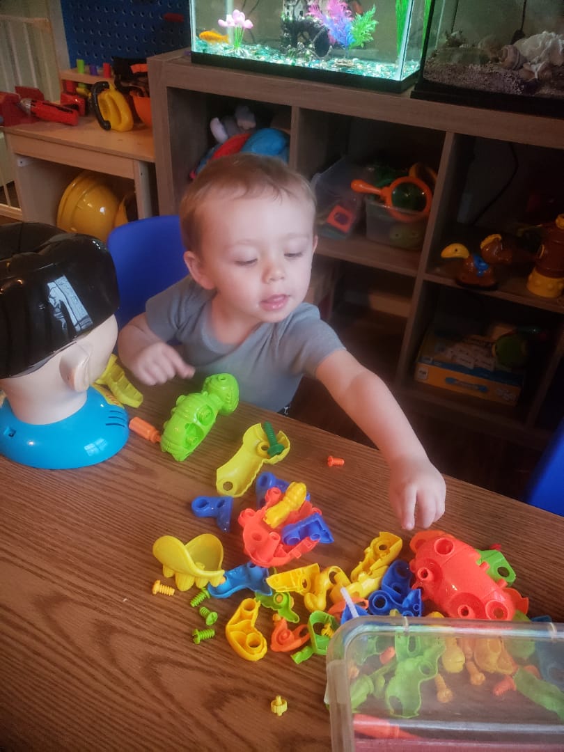 A toddler concentrating on colorful building manipulatives beside the classroom fish tank